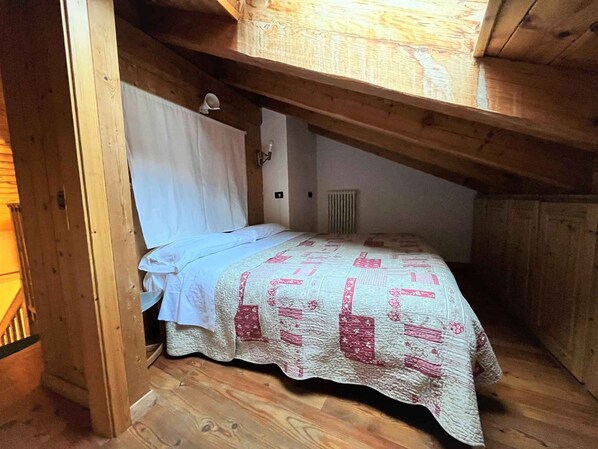 A small, cozy attic bedroom with a wooden ceiling and sloped roof.
