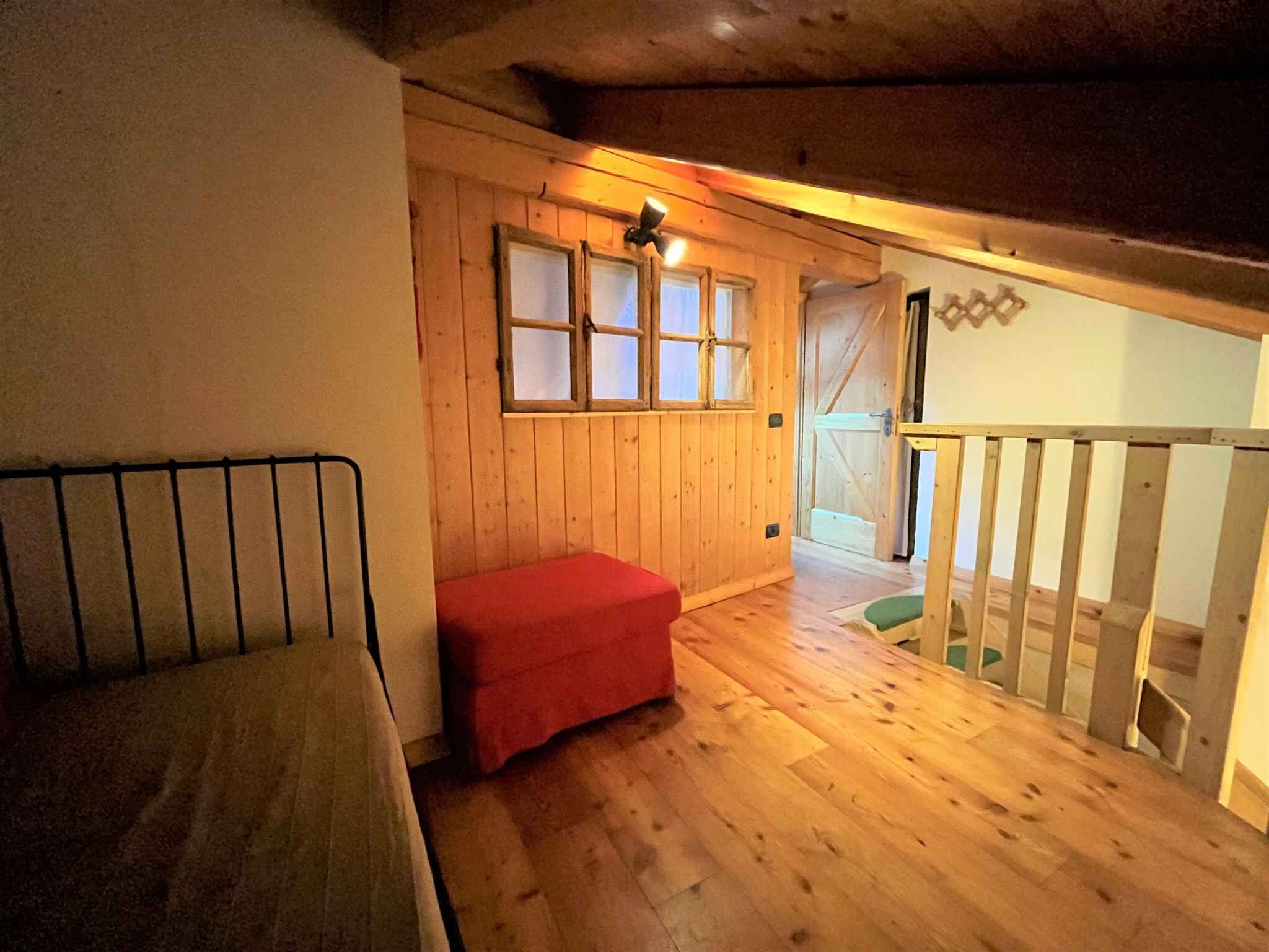 Un interior de madera con una cama, un banco rojo y una escalera.