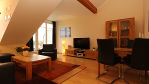 A modern living room with a wooden ceiling, a TV, a dining table, and black chairs. - Whg.14, 2nd floor, 2-room, Zinnowitz - Residence Bellevue Fewos Arts - Fewo.cc (Zinnowitz)