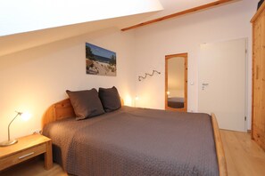 Une chambre à coucher comprenant un lit, une table de chevet, une lampe fixée au mur, une porte et une armoire en bois.