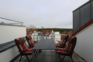 Un balcon avec une table et quatre chaises, donnant sur une rangée de maisons aux toits rouges.