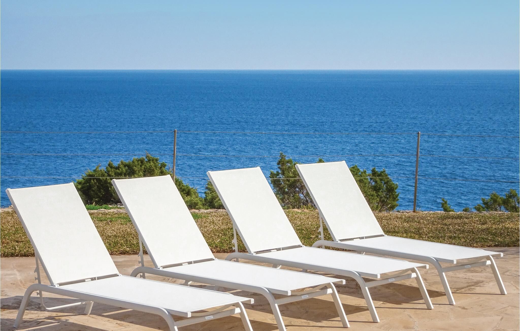 Three white lounge chairs with metal frames, positioned on a patio overlooking a body of water.