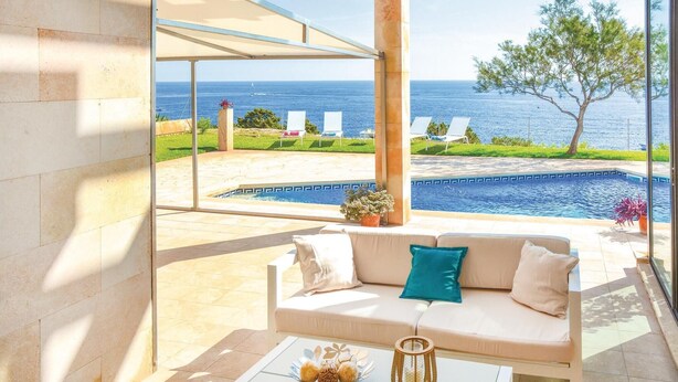 A sunlit outdoor seating area with a view of the sea and a swimming pool. - Gorgeous home in Porto Colom (Porto Colom)