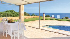 A covered outdoor dining area with a table set for two, overlooking a swimming pool and the sea.