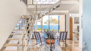 A modern interior with a staircase leading to an upper level, a dining area with a view, and a large window overlooking the sea. - Gorgeous home in Porto Colom (Porto Colom)
