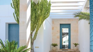 A modern building with a white exterior, a blue door, and a large cactus in the center. - Gorgeous home in Porto Colom (Porto Colom)