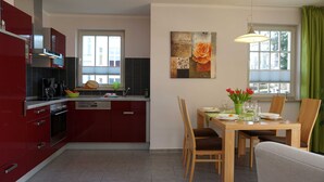 Eine moderne Küche mit roten Schränken, ein Essbereich mit einem Holztisch für vier Personen und einem grünen Vorhang.