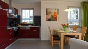 Una cucina moderna con mobili rossi, un'area pranzo con tavolo in legno apparecchiata per quattro persone e una tenda verde.