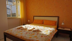 Ein Schlafzimmer mit einem Bett, zwei Kissen, einem Nachttisch, einer Lampe und einem Fenster mit Vorhängen.