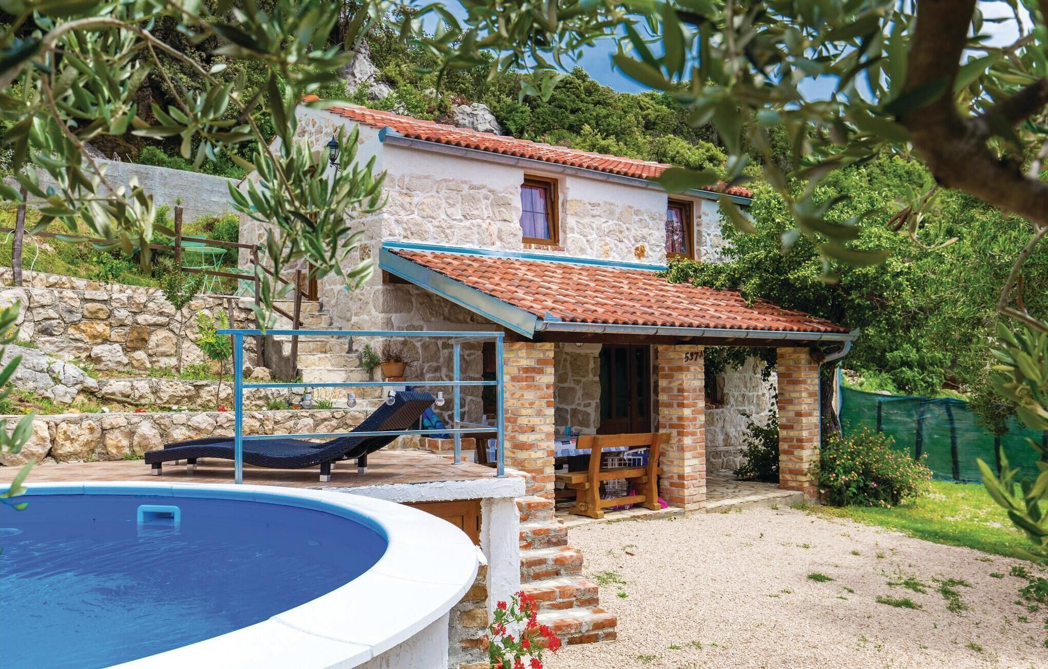 Une maison en pierre avec un toit en tuiles, une piscine et un petit espace extérieur aménagé pour s’asseoir.