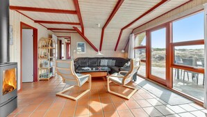 Une pièce chaleureuse avec une cheminée, un canapé et une grande fenêtre donnant sur la plage.