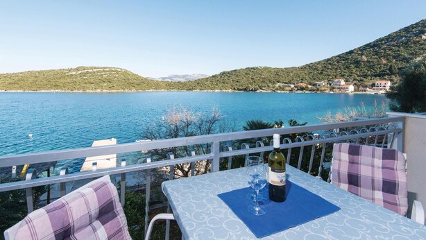 A balcony with a table set for two, overlooking a body of water and a hillside with buildings. - Gorgeous apartment in Dubrava with house sea view (Dubrava)
