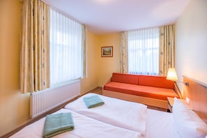 A hotel room with two beds, a sofa, a radiator, and a picture on the wall.