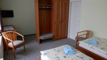Une chambre avec deux lits simples, une armoire en bois, une chaise et un bureau.