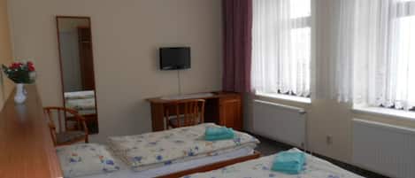 A room with two beds, a desk, a chair, a television, and a window with curtains.