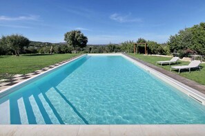 Una piscina rettangolare con acqua cristallina, circondata da un prato e alberi.