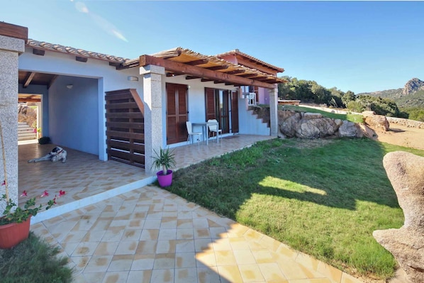 Una casa con portico coperto, muro in pietra e giardino lastricato.