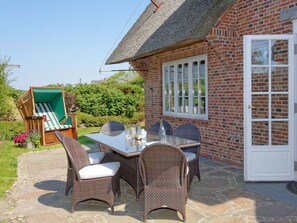 A brick house with a thatched roof, a dining table with wicker chairs, and a garden with a swing set. - Prahl Hüs 5 from A&M - Prahl Hüs 5 (Kampen (Sylt))