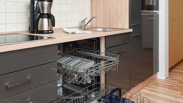 Eine moderne Küche mit schwarzen und hölzernen Schränken, einem eingebauten Geschirrspüler und einer Kaffeemaschine.