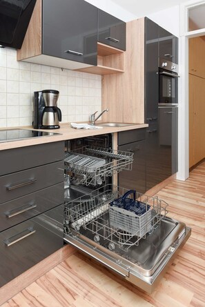 A modern kitchen with black and wooden cabinets, a built-in dishwasher, and a coffee maker.