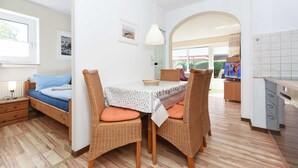 Ein gemütliches Zimmer mit einem Bett, einem Esstisch mit Korbstühlen, einem Fernseher und einer Küchenzeile.