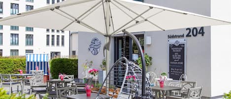 En udendørs café med borde og stole, en stor parasol og et skilt, der angiver, at stedet er nummer 204.