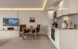 A modern kitchen with a dining area, featuring a flat-screen TV, a painting, and a coffee maker.