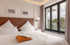 A hotel room with a large bed, two pillows, a nightstand, a lamp, and a window with curtains.