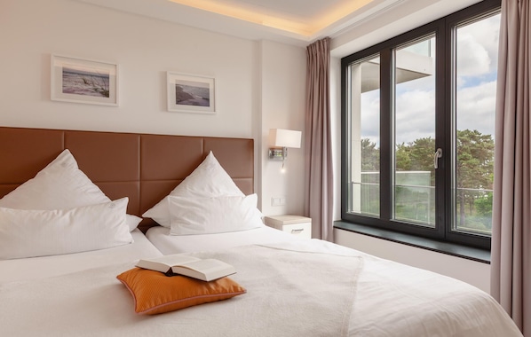 A hotel room with a large bed, two pillows, a nightstand, a lamp, and a window with curtains.