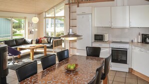 Cozinha moderna com armários brancos, micro-ondas e fogão. Possui área de jantar com mesa e cadeiras, e um sofá.
