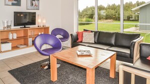 Uma sala de estar moderna com uma mesa de centro de madeira, duas cadeiras roxas, um sofá de couro preto e uma televisão sobre um móvel de madeira.