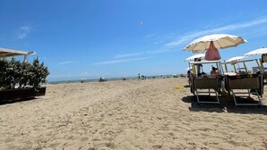 A beach with sun umbrellas, lounge chairs, and a clear blue sky. - Happy Camp in Camping Laguna Village (Caorle)