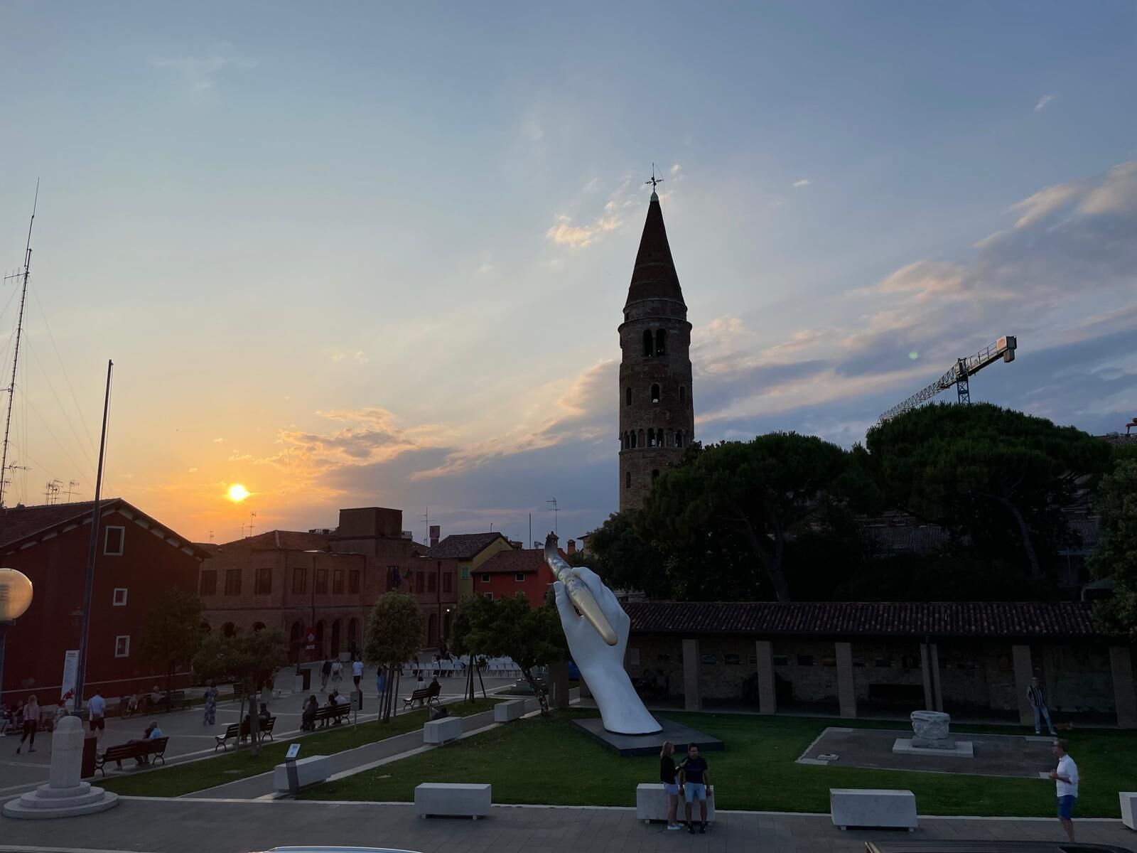 A public square with a large sculpture, a tower, and a sunset.