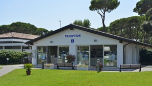 A reception building with a sign, a bench, and a potted plant in the foreground. - Happy Camp in Camping Laguna Village (Caorle)