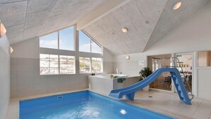 Ein Hallenbad mit blauer Rutsche, großen Fenstern und Blick auf den Strand.