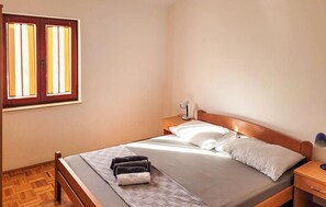 Un dormitorio con cama, mesita de noche, lámpara y ventana con cortinas.