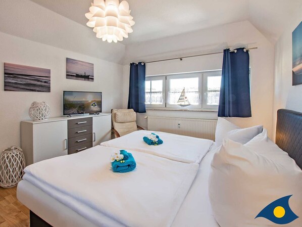 A hotel room with two beds, a TV, a window with curtains, and artwork on the walls.