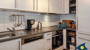 A modern kitchen with white cabinets, a stainless steel sink, a coffee maker, and an oven. - Villa Maria - Gabriele Whg. 13 - Maria 13 (Loddin)