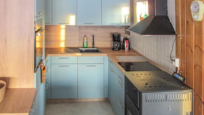 Una cocina compacta con gabinetes azul claro, un lavamanos de acero inoxidable, una cafetera y una campana extractora.