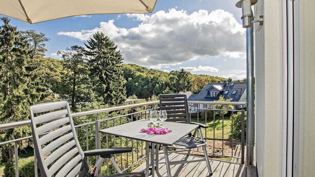 Un balcon avec une table et des chaises, un verre de vin et une fleur.