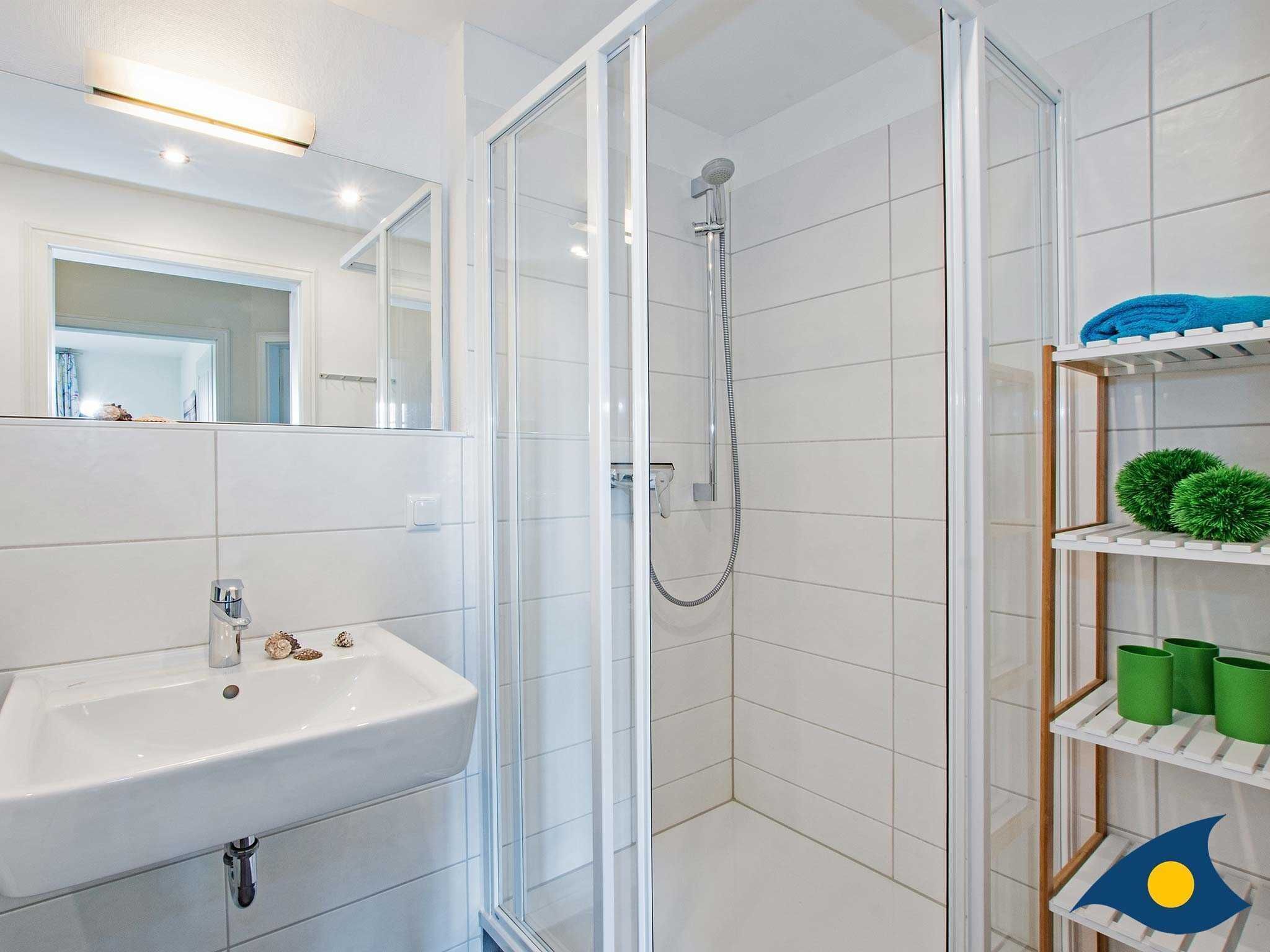 A bathroom with a white sink, a glass-enclosed shower, and a shelf with green and blue items.