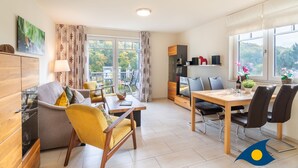 Un salon moderne avec un canapé, un fauteuil jaune, une table à manger et des chaises. On y trouve également un téléviseur, un meuble et une fenêtre avec des rideaux.