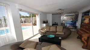 Un salon avec un canapé, une table basse et un piano. On peut apercevoir une piscine à travers les portes vitrées.