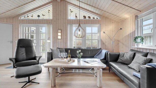 Ein geräumiger Wohnbereich mit hoher Decke, Holzwänden, einem schwarzen Ledersofa, einem grauen Couchen und einem schwarzen Ledersessel.