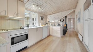 Eine moderne Küche mit Holzausstattung, einem eingebauten Ofen, einem Herd und einem großen Fenster für natürliches Licht.