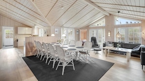 Ein geräumiger, gut beleuchteter Raum mit hohen Decken, einem Essbereich mit rundem Tisch und weißen Stühlen, einer schwarzen Couch und einem großen Fenster, das für natürliches Licht sorgt.