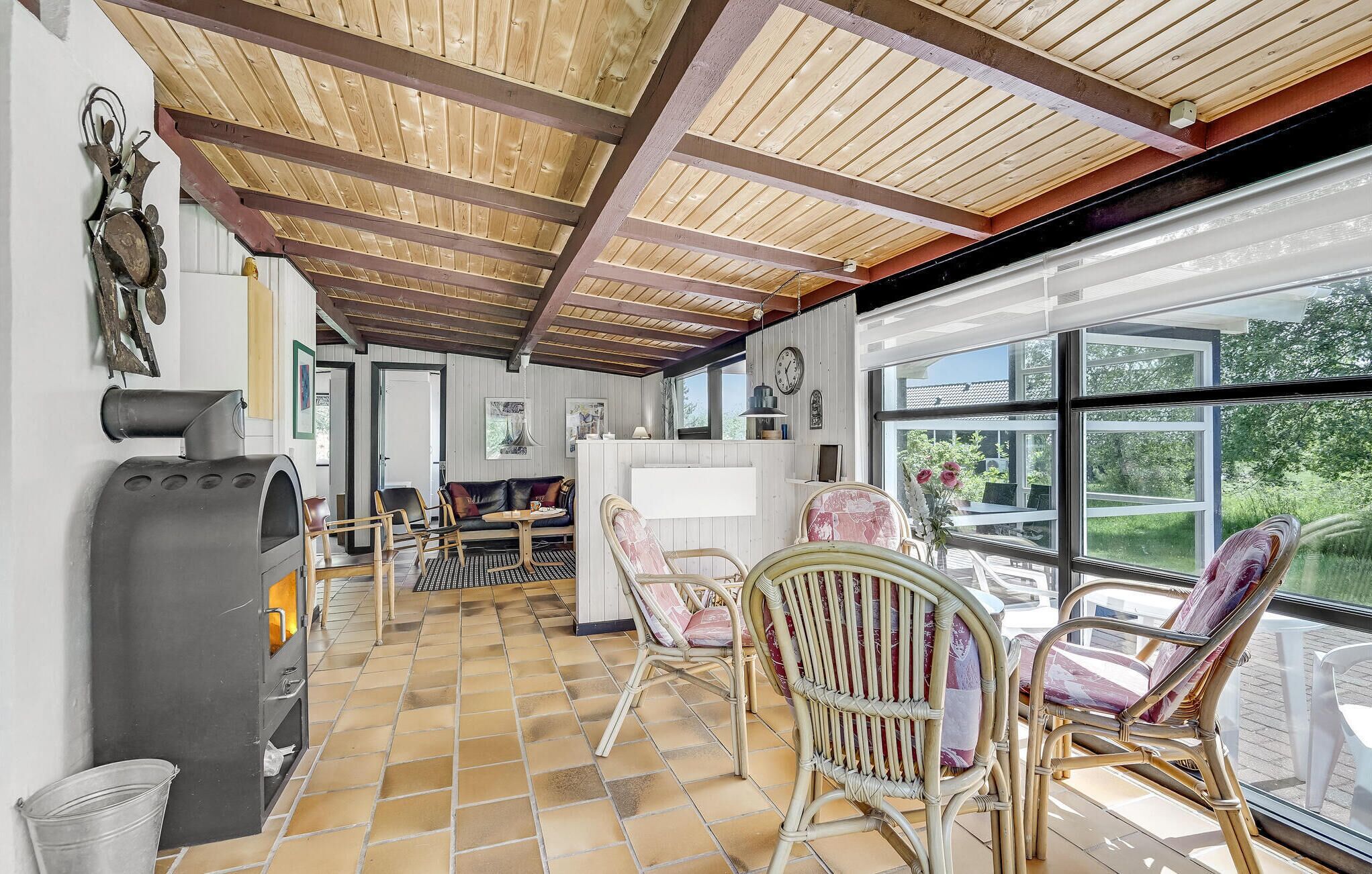 A spacious patio area with wooden beams, wicker furniture, and a large window offering a view of greenery.