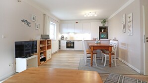 Una cocina moderna con armarios blancos, un comedor con mesa y sillas de madera, y un televisor sobre un mueble.