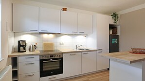 Una cocina moderna con armarios blancos, horno empotrado, cafetera y pileta.