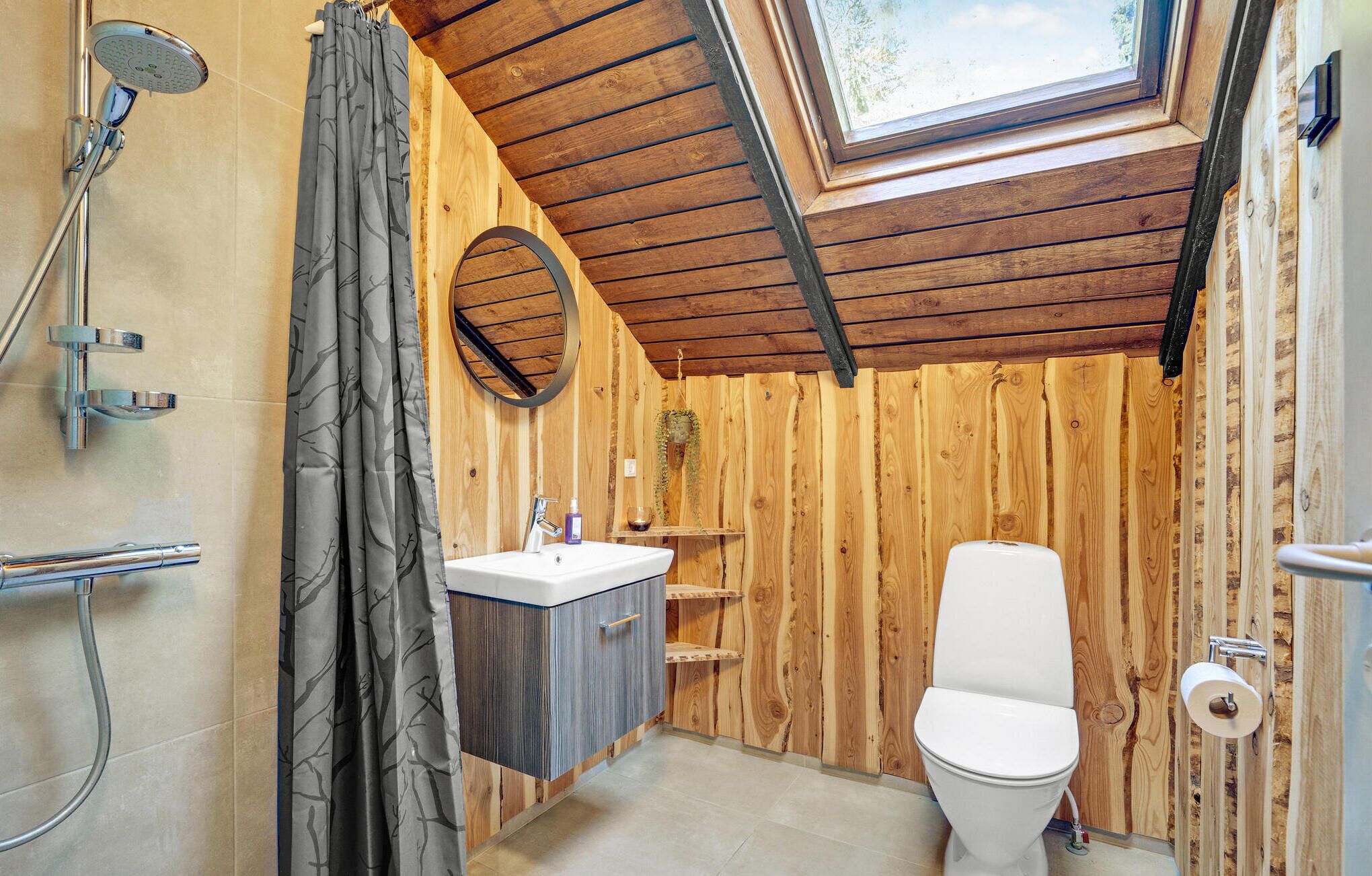 A compact bathroom with a skylight, wooden walls, a shower, a toilet, and a sink.